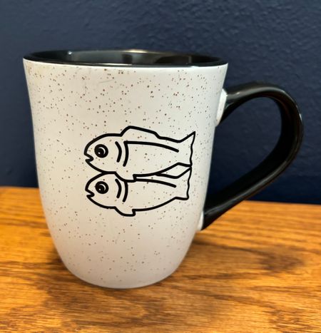 A mug printed with a black & white outline of two fish stacked facing left, which is the Glitch logo
