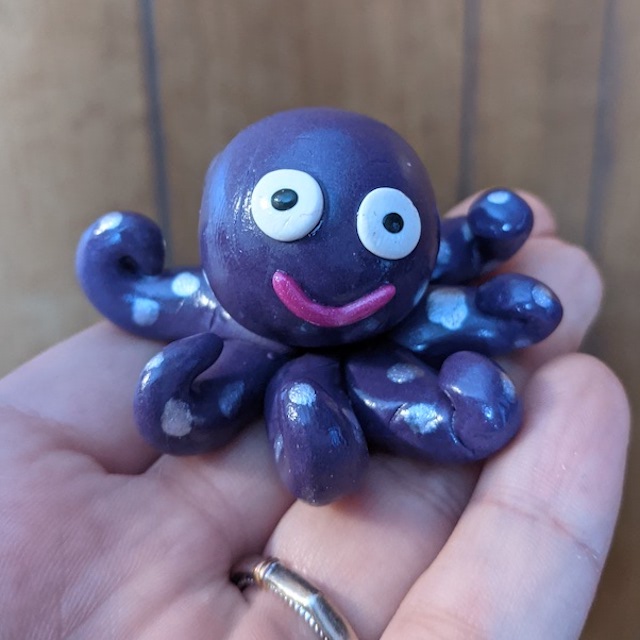 a shiny purple octopus with painted on spots on the tentacles and big eyes and a smile sits on an outstretched hand