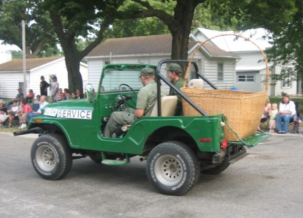 a green jeep with open sides and top has a gigantic picnic basket in the back