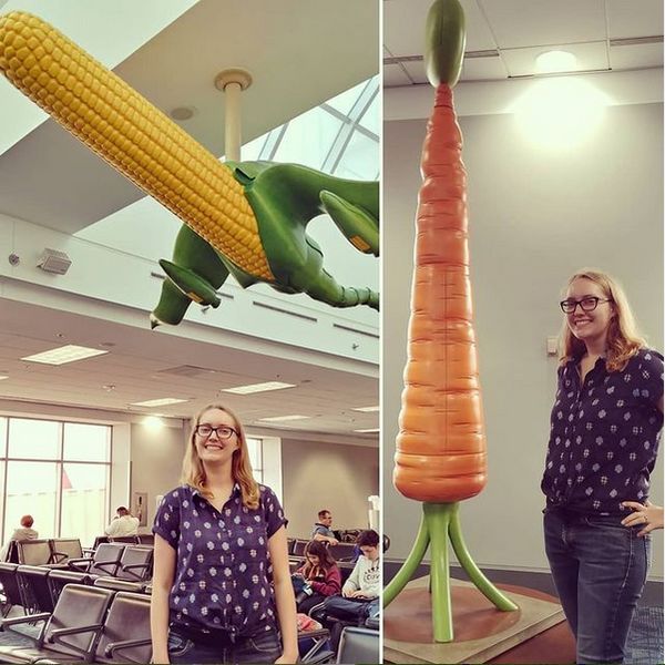two images side by side: one of Cassey standing under a sculpture of corn in the shape of an airplane hanging from the ceiling of an airport waiting room, the other of Cassey standing proudly next to a carrot in the shape of a rocket about to blast off